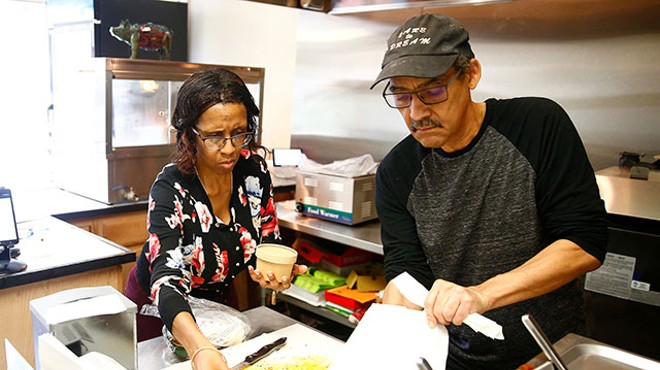 A Black man and woman pack up food in the kitchen of a restaurant.