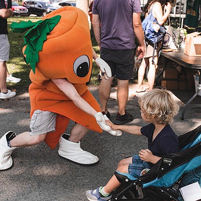 A person dressed up as a carrot high fives a young child in a stroller