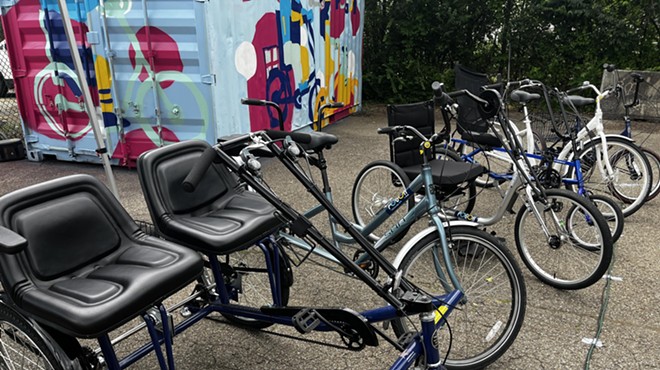 Tricycles and hand-crank bicycles with POGOH stickers sit near a spray-painted shipping container
