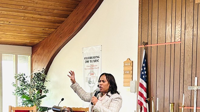 A woman speaks in a historic church while the pastor looks on