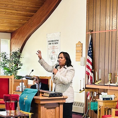 A woman speaks in a historic church while the pastor looks on