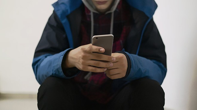 A person in a hoodie holds a phone in their hands. Their face is not visible.