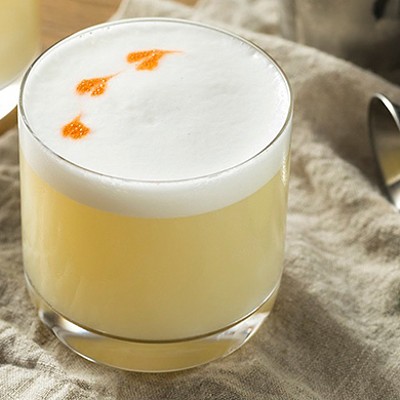 A pretty Pisco Sour cocktail with white foam on top sits on a table.