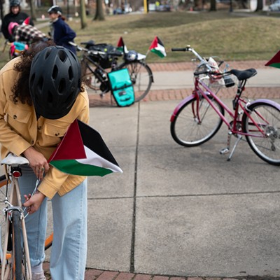A person with long hair covered by a bike helmet mounts a Palestinian flag to their seatpost tube