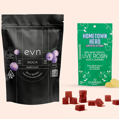 Pale pink background, image of black bag labeled "evn indica bubba kush wild berry", green bag labeled "hometown hero supporting veterans 100% hemp derived live rosin indica gummies", with dark red gummies scattered in the foreground