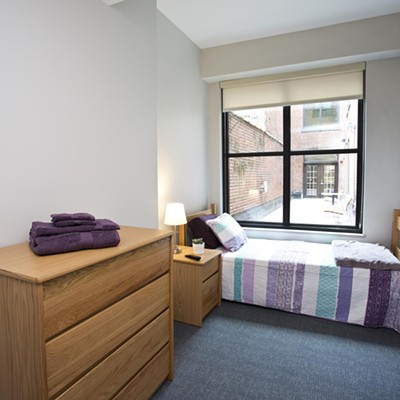 A spacious bedroom with dorm-style wooden furniture and a wall-mounted TV