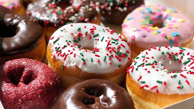 An assortment of brightly colored donuts cover in various icings, including rainbow-colored sprinkles on white icing, chocolate icing, and pink icing