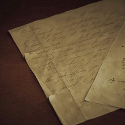 A photo of two letters, both handwritten in script on beige paper, on a brown background