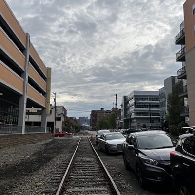 Aging railroad tracks run among high-density development with cars parked alongside them in the Strip District.