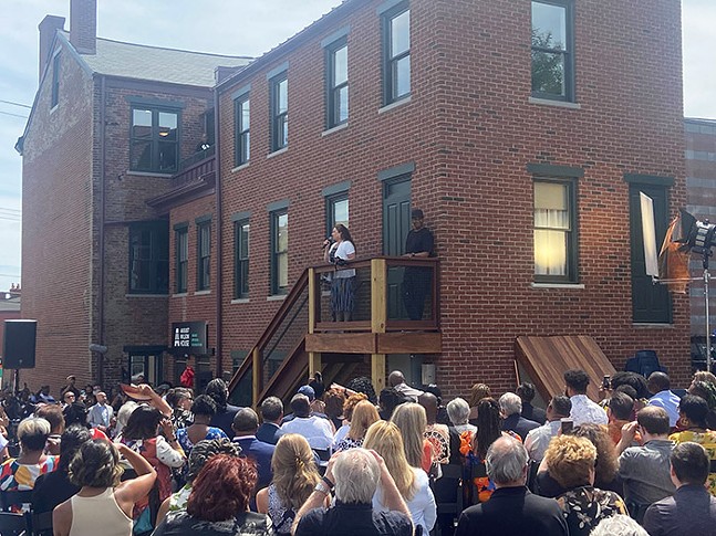 A large crowd of people watch as a woman and a man stand on the steps of a red brick building