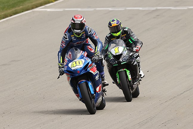 Two adults ride motorcycles side by side on a racetrack