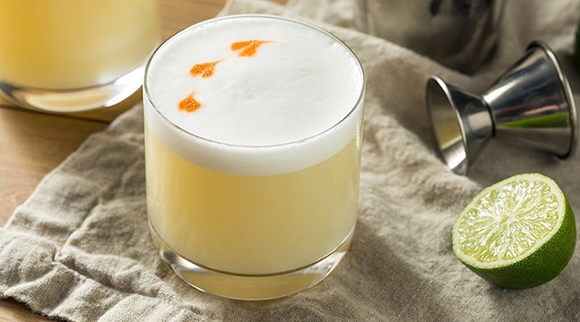 A pretty Pisco Sour cocktail with white foam on top sits on a table.
