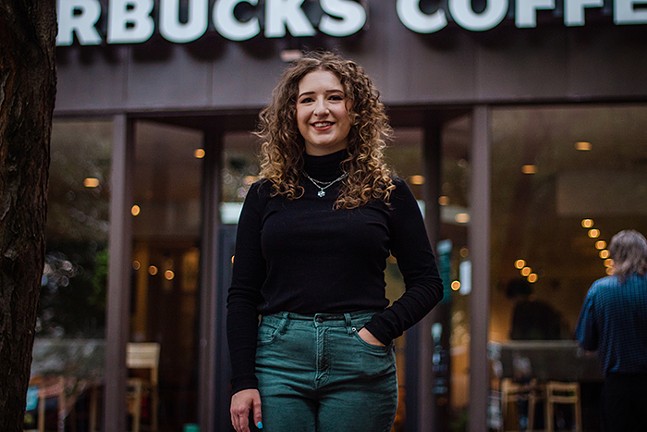 A woman smiling in front of a store with a "Starbucks Coffee" sign above the door