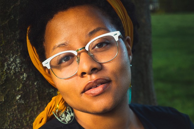 A close-up of Black playwright a.k. payne wearing glasses and a colorful head scarf.