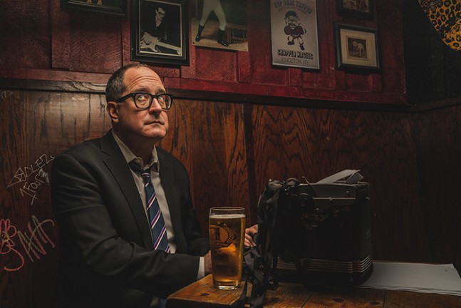 A man sits in a booth with a beer and typewriter