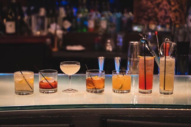 A line of cocktails are set up on top of a lit bar.