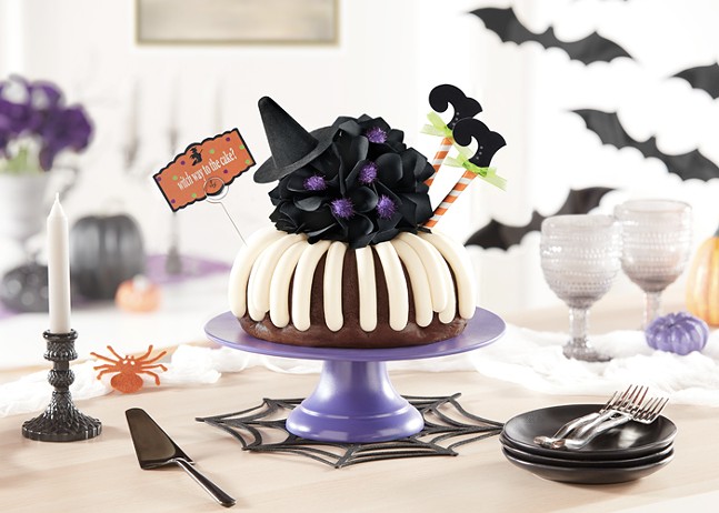A bundt cake decorated with witch legs and a little witch hat sits displayed on a festive Halloween table.