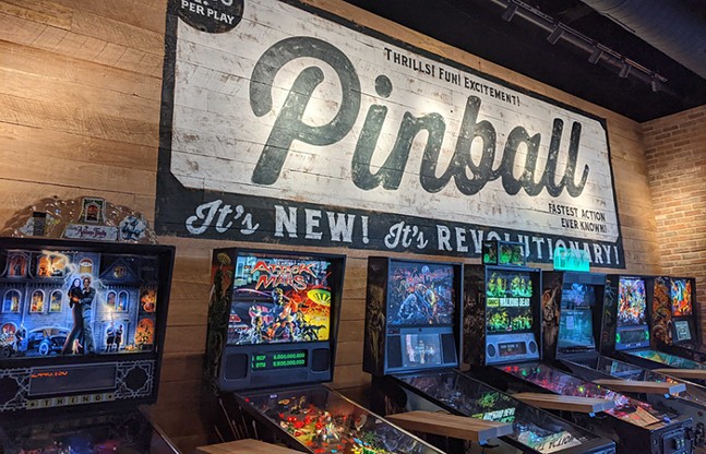 A line of colorful pinball machines line a wall at Pins Mechanical.