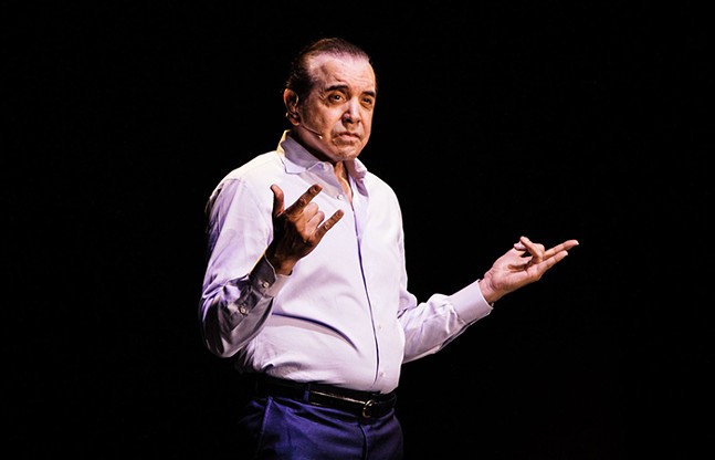 A man stands on stage in a dress shirt and pants