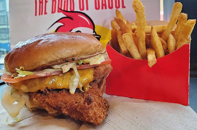 A large fried chicken sandwich sits next to a bright-red box of french fries.