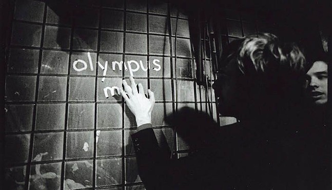 Black and white photo where a man writes "olympus m-" in the dust