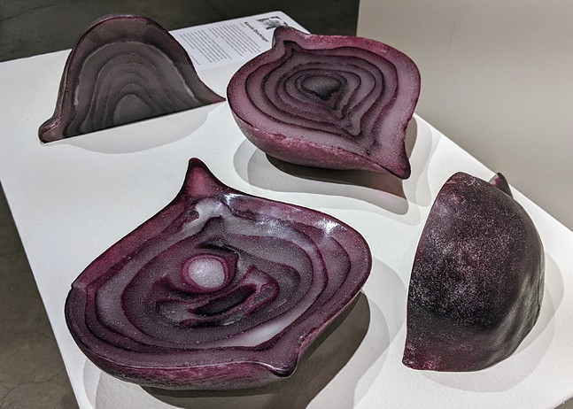 A giant red onion made of glass sits on a pedestal in an art gallery.