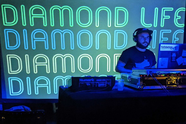 A DJ plays in front of a projection screen that read "Diamond Life" in big letters.