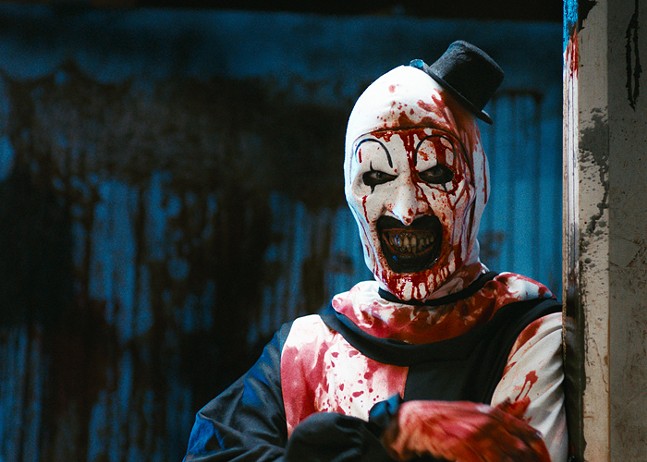 A scary clown in black and white makeup covered in blood.