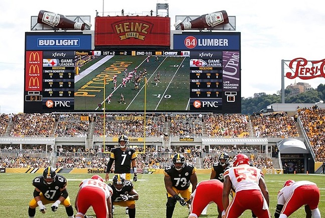 Two football teams, one wearing black and gold uniforms and the other wearing red and white uniforms, get into position at the former Heinz Field in Pittsburgh.