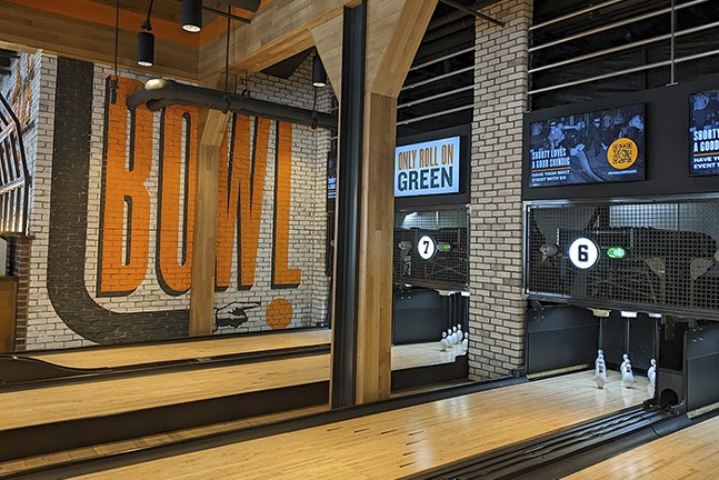 Stubby pins sit at the end of bowling lanes in a spacious, industrial-style bar.