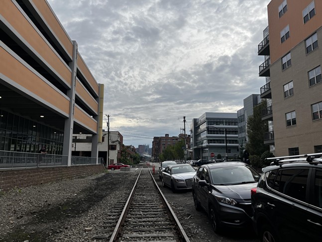 Aging railroad tracks run among high-density development with cars parked alongside them in the Strip District.