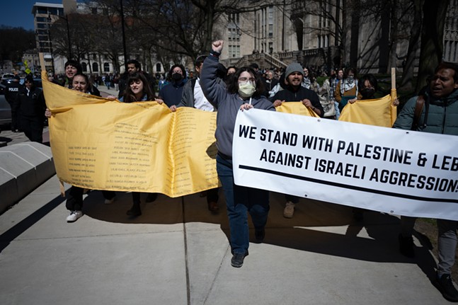 Protestors in masks hold a banner with names and sign proclaiming a pro-Palestine and Lebanon stance