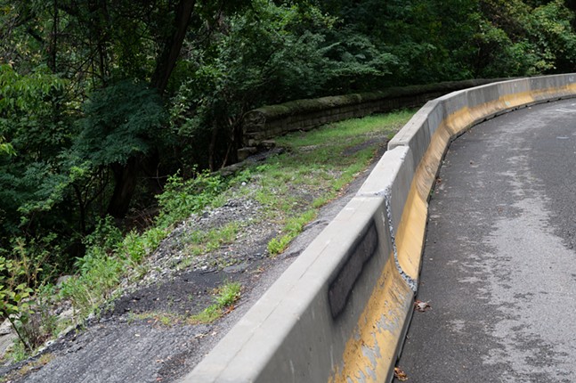 Behind a jersey barrier, a stone wall holding back an embankment lies broken