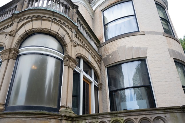 Curved and stained glass windows adorn the intricate brick façade of a mansion