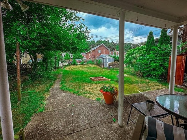 A long grassy lot with a brick firepit and covered patio