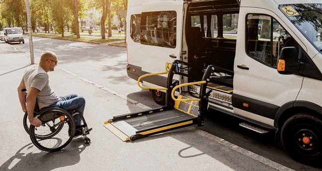 A wheelchair user with sunglasses and shaved head rolls onto a ramp to get into an accessible van