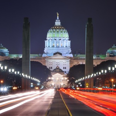 Harrisburg capitol building lit up at night, with a dark sky and bright white and red lights on the street