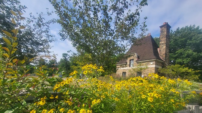 Bright yellow flowers overflow along a wood fence near a high-roofed stone gatehouse